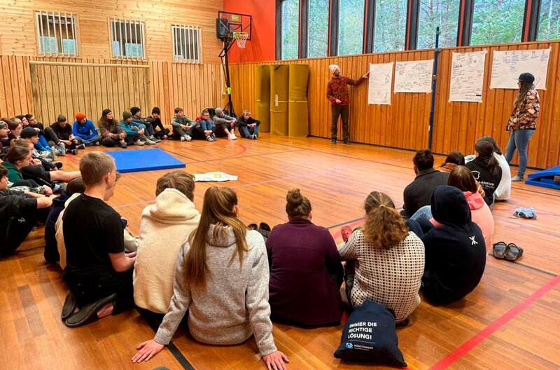 Flo von der Huskyfarm informiert die Schülerinnen und Schüler über die wichtigsten Dinge zur bevorstehenden Husky Tour nach Kvinen. Weiteres Bildmaterial finden Sie unter www.br-foto.de. – Bild: BR/​Bewegte Zeiten Filmproduktion GmbH/​Megan Ehrmann