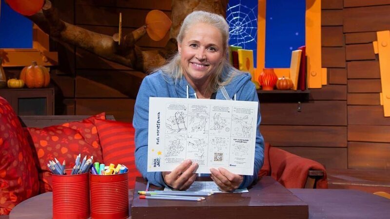 Es ist MACH-MiT!-Woche im Baumhaus. Singa stellt den Bastelbogen für diesen Monat vor und hat schon das Deckblatt für das Minibuch gestaltet. – Bild: KiKA