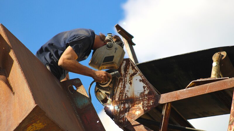 Cousin Mike schweißt am Förderband fest. – Bild: Warner Bros. Discovery, Inc. or its subsidiaries and affiliates