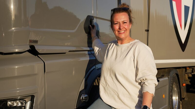 E01 – Samantha next to the cabin smiling, right arm on the door, right leg up the bumper, twisted to her left to the camera, medium shot – Bild: Warner Bros. Discovery, Inc. or its subsidiaries and affiliates