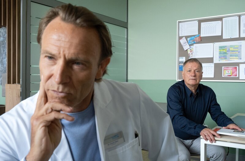 Dr. Martin Steins (Bernhard Bettermann, li.) Patientin verweigert trotz starker Bauchschmerzen jede weitere Diagnostik. Da sie aus dem Gefängnis überwiesen wurde, vermutet Martin, dass sie etwas schmuggeln will. Doch Dr. Roland Heilmann (Thomas Rühmann) glaubt das nicht. – Bild: MDR/​Saxonia Media/​Sebastian Kiss