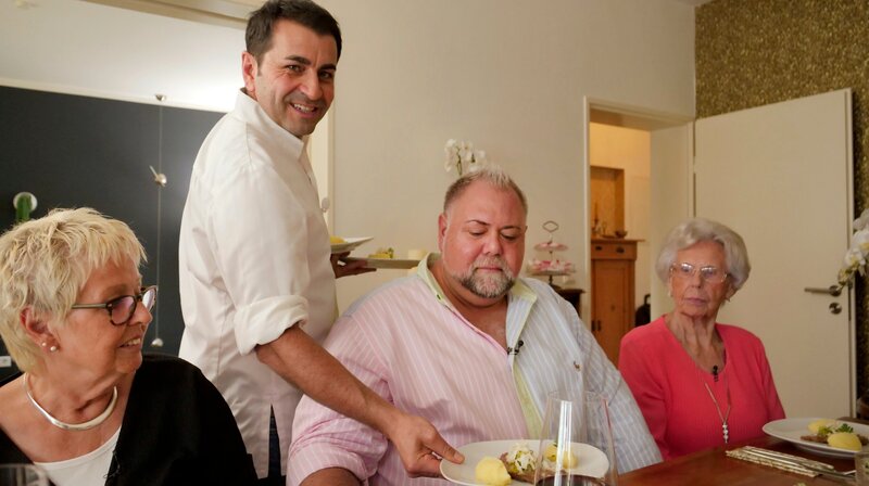 Profikoch Ali Güngörmüs (stehend) serviert Sven Maximilian Seib und dessen Mutter Ingrid Seib (links) sowie dessen Großmutter Marianne Winiarek seine Neuinterpretation eines Traditionsgerichts. – Bild: HR/​Jonas Heil