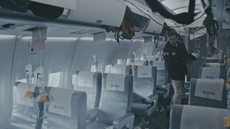 NTSB-Ermittler (gespielt von Chris Violette) untersuchen die schwer beschädigte Passagierkabine von China Eastern Airlines Flug 583 auf Hinweise, die erklären könnten, warum die MD-11 plötzlich in eine Reihe heftiger Schwingungen geriet, die so stark waren, dass zwei Passagiere getötet und mehr als 100 weitere verletzt wurden. – Bild: Cineflix