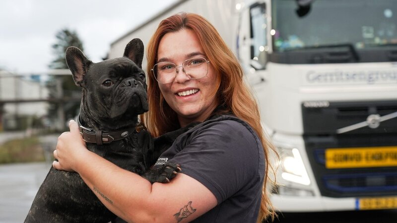 Ep10 – Louise twisted to her left to the camera, in front of her truck holding her dog, truck to the right of the frame, smiling – Bild: Warner Bros. Discovery, Inc. or its subsidiaries and affiliates. All rights reserved.