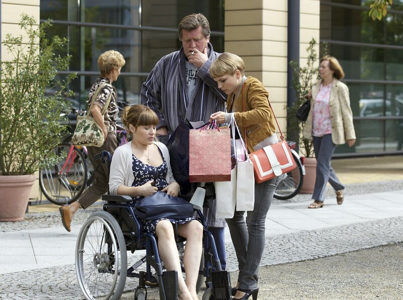 Natalie Lange (Anna Hopperdietz, re.) bringt ihre Schwester Claudia (Daniela Preuß, li.) in die Sachsenklinik, weil sie über Unterleibsschmerzen klagt. Widerwillig nimmt Claudia das Angebot eines Patienten (Bruno F. Apitz, mi.) an und setzt sich in seinen Rollstuhl. – Bild: MDR/​Wernicke