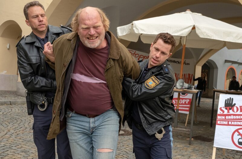 Peter Pfitzer (Ferdinand Dörfler, M.), Chef einer Bürgerinitiative, die vehement gegen die Modernisierung des Lifts protestiert, gerät unter Mordverdacht und wird von den Berchtesgadener Polizisten abgeführt. V.l.n.r. Komparse, Peter Pfitzer (Ferdinand Dörfler), Max Ruffer (Nepo Fitz) – Bild: ARD/​Raymond Roemke