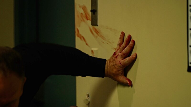 Ein Mann klammert sich mit einer blutigen Hand an die Wand – Bild: ZLW-S2-blackwatch /​ © Crime + Investigation