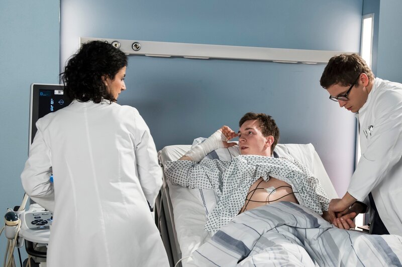 Oliver ist geschockt, dass er in seinem jungen Alter schon unter regelmäßigen Herzinfarkten leidet. V.l.n.r. Dr. Leyla Sherbaz (Sanam Afrashteh), Oliver Schuster (Johannes Kienast), Elias Bähr (Stefan Ruppe). – Bild: ARD/​Jens Ulrich Koch