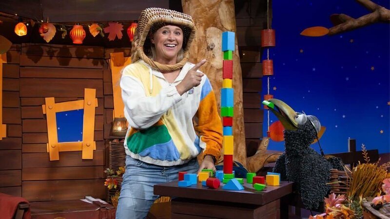 Rudi ist zu Besuch im Baumhaus und baut mit Singa einen wackeligen Turm aus bunten Klötzen. Dabei schützen sie sich mit lustigen Helmen auf ihren Köpfen. – Bild: KiKA