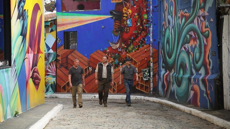 Josh Gates, Mike Lynch und Ken Wilder spazieren durch Sao Paulo, Brasilien, auf dem Weg zu einem Treffen mit einem örtlichen Ermittler. – Bild: Warner Bros. Discovery