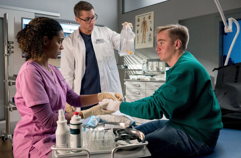 Dr. Elias Bähr (Stefan Ruppe) und Dr. Emma Jahn (Elisa Agbaglah) versorgen Tim Gillich (Philipp Franck), ein Patient mit rätselhaft geschwollenen Händen. – Bild: ARD/​Jens-Ulrich Koch