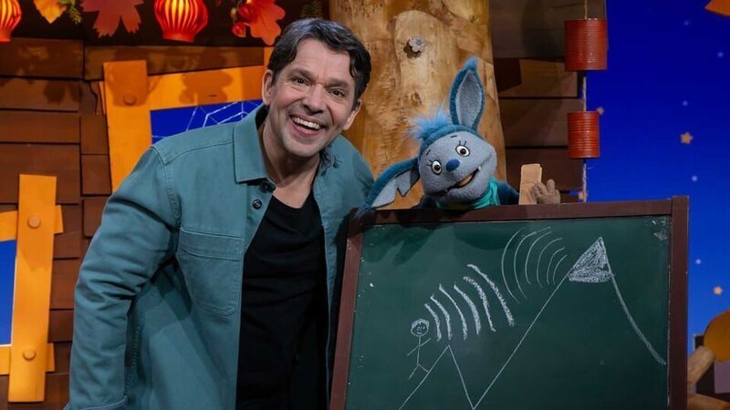 Juri erzählt von seiner Herbstwanderung und erklärt was ein Echo ist und wie es funktioniert. Fidi hört gespannt zu. – Bild: KiKA