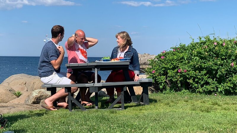 Contributors Will Sweet (L) and Bob Gentile (C) sit with Wendy Fox (R) and learn the best way to crack into a Maine lobster as seen on HGTV’s Beachfront Bargain Hunt. – Bild: Discovery, Inc.