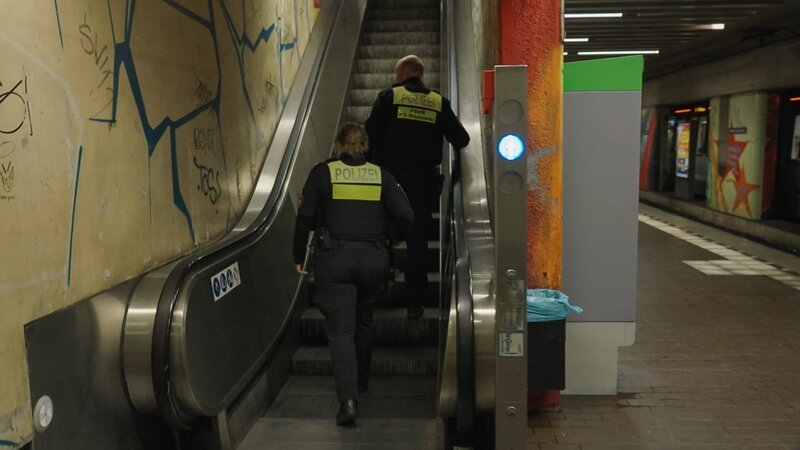 Polizisten steigen die Rolltreppe hinauf. – Bild: Warner Bros. Discovery