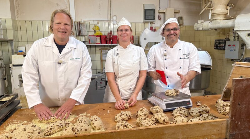 In der Stollenproduktion von Bäcker Jörg Liese (r) und seiner Mitarbeiterin Christiane Middel packt Björn Freitag tatkräftig mit an. – Bild: Joshua Stolz