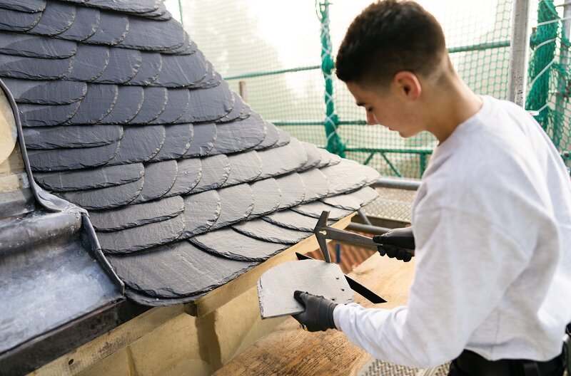 Simeon (Foto, 16) arbeitet heute auf „Haus Stapel“, einem imposanten Wasserschloss. Zusammen mit den Dachdecker-Gesellen Nick und Martin reißt er das Schieferdach ab. – Bild: WDR/​Ben Knabe