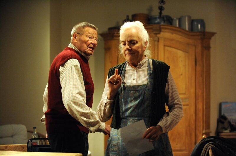 Theres hat Alois gebeten, das kaputte Scharnier zu reparieren. Von links: Alois Preissinger (Erich Hallhuber) und Theresa Brunner (Ursula Erber). – Bild: Bild: BR/​Marco Orlando Pichler