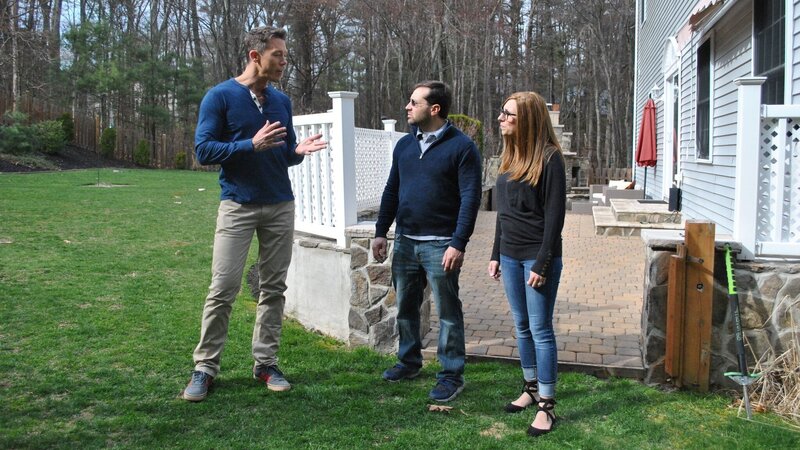 David Bromstad in a blue sweater, explains house details to the winners, by the backyard and outdoor area, one possible house – Bild: HGTV