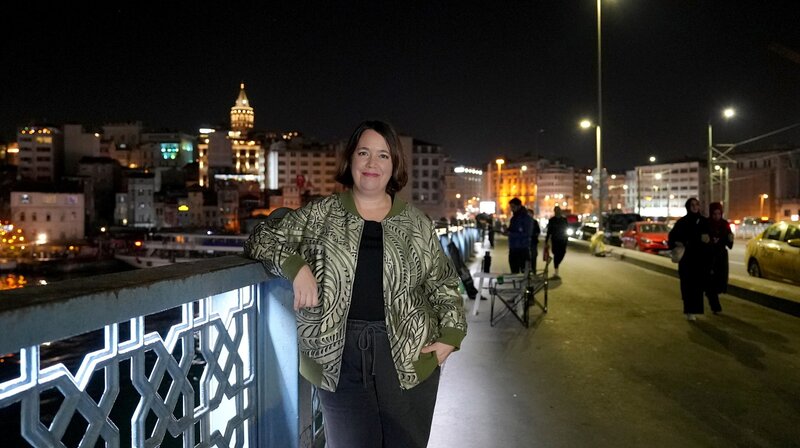 Phoebe Gaa steht auf einer der Brücken in Istanbul und schaut lächelnd in die Kamera. Im Hintergrund liegt die Stadt bei Nacht. – Bild: phoenix/​ZDF/​Zeljko Pehar