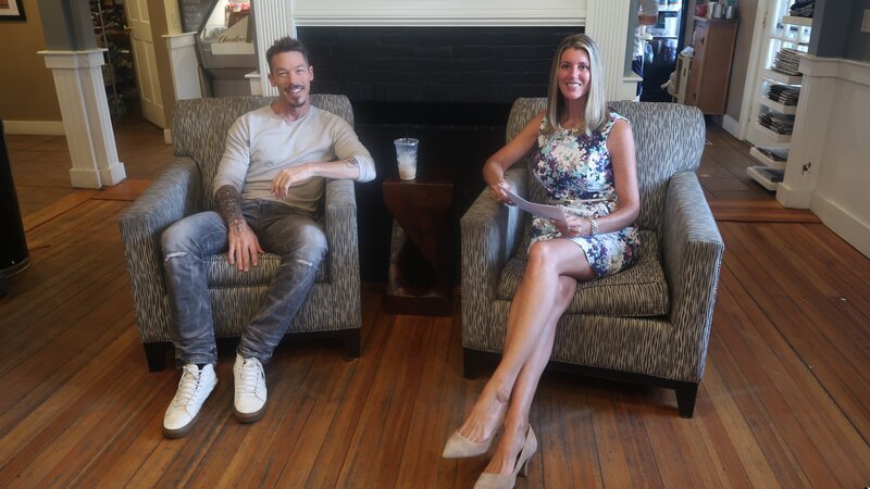 David Bromstad, in a grey tshirt , is welcomed by the real estate agent at his.prefered coffe shop – Bild: HGTV/​Scripps Networks, LLC. All Rights Reserved