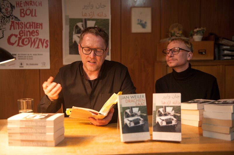 Der Autor Jan Weiler bei seiner Lesung im Institut zusammen mit Titus (Robert Stadlober), der die Fragerunde eröffnet. – Bild: BR/​Novafilm Fernsehproduktion GmbH/​Alva Nowak