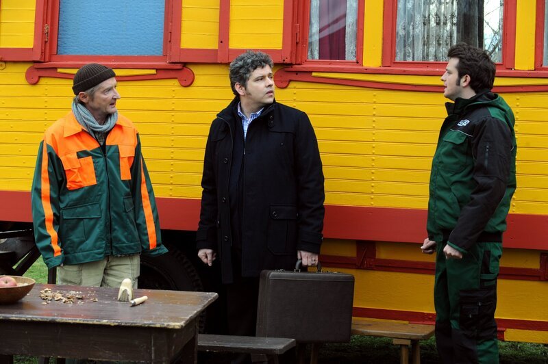 Flori bekommt erschrocken mit, dass ein GEZ-Beauftragter mit Xaver sprechen will. Von links: Xaver (Michael Schreiner), GEZ-Beauftragter (Rudi S. Gall) und Florian Brunner (Tommy Schwimmer). – Bild: BR/​Marco Orlando Pichler