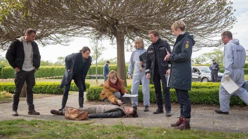Hundetrainerin Christin Neuhaus (Lena Görgens) ist im Park von einem Unbekannten mit Pfefferspray attackiert worden. Kommissar Lars Pöhlmann (Dominic Boeer, l.), Kommissarin Joost (Nike Fuhrmann, 2.v.l.), Rechtsmedizinerin Dr. Helene Sturbeck (Katharina Blaschke, 3.v.l.), Roswitha (Silke Matthias, m.), Timmermann (Mathias Junge, 3.v.r.) und Stine (Sidsel Hindhede, 2.v.r.) fragen sich: Ist die junge Frau gezielt mit Pfefferspray attackiert worden, um eine allergische Reaktion hervorzurufen? – Bild: ZDF/​Meyerbroeker