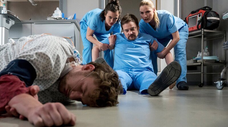 Linus Haas hat sich bei dem Sturz aus seinem Patientenbett verletzt und ist ohnmächtig. Dr. Lindner eilt zur Stelle, doch es geschieht etwas Ungewöhnliches. Rebecca Krieger und Julia Berger greifen ein. – Bild: ARD/​Jens-Ulrich Koch
