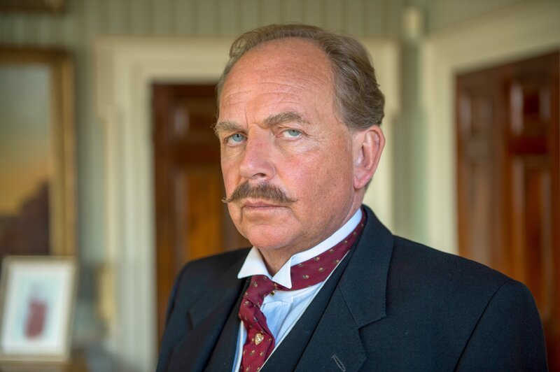 „Agatha Christie’s Poirot“, „Die Arbeiten des Herkules.“ Hercule Poirot hat Besuch – Dr. Burton, ein Fellow des All Souls Colleges in Oxford. Die Konversation dreht sich um den ungewöhnlichen Vornamen von Poirot und darum, dass manchmal der von den Eltern gegebene Vorname nicht zu den Kindern passt. Dr. Burton zitiert aus Homers Ilias (XXIII, 316 f.) und erzählt dann Poirot die Sage von Herakles. Poirot gibt zu, diese nicht zu kennen, weil er keine Zeit hatte, die alten Sprachen zu studieren. Später verkündet Poirot, dass er sich nach ein paar noch zu lösenden Fällen in den Ruhestand begeben wolle. Burton regt lachend an, die Fälle nach den zwölf Arbeiten des Herkles zu benennen. Nachdem er eine Nacht darüber nachgedacht hat, entscheidet sich Poirot, die Idee umzusetzen. Im Bild: Patrick Ryecart (Sir Anthony Morgan). – Bild: Neil Genower /​ ORF /​ ITV Studios Global Entertainment