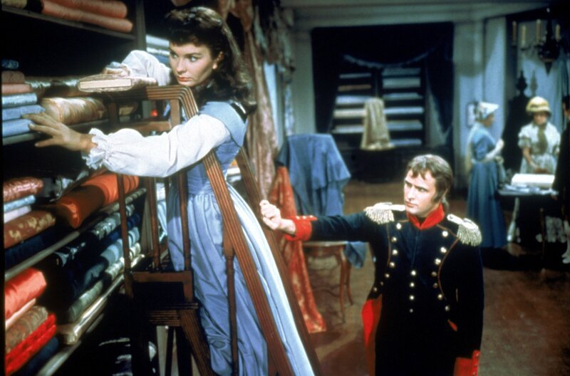 Napoleon Bonaparte (Marlon Brando) besucht seine Geliebte Désirée (Jean Simmons) im familieneigenen Geschäft, wo sie Stoffe für ein Hochzeitskleid auswählt. – Bild: Twentieth Century Fox Film Corporation