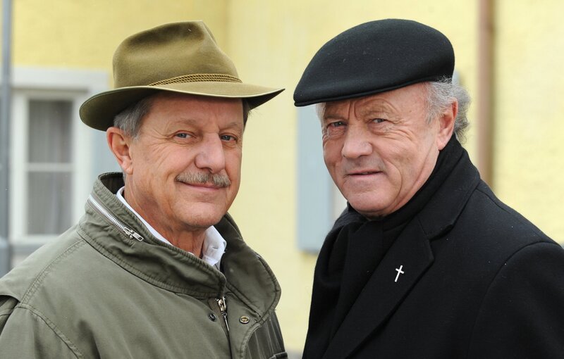 Der Bürgermeister und der Pfarrer wollen ab sofort an einem Strang ziehen. Von links: Bürgermeister Schattenhofer (Werner Rom) und Pfarrer Kurz (Hans Stadlbauer). – Bild: BR/​Marco Orlando Pichler