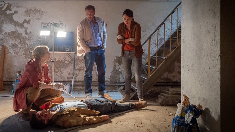 Der Handwerker Hendrik Reschke (André Borning, liegend) hat in liebevoller Kleinarbeit ein altes Kontorhaus in Wismars Innenstadt saniert. Doch die Bauarbeiten werden jäh unterbrochen, als sein Mitarbeiter ihn tot am Fuße einer Treppe im Keller des Hauses auffindet. Ein neuer Fall für die Kommissare Joost (Nike Fuhrmann, r.) und Pöhlmann (Dominic Boeer, M.) oder nur ein tragischer Unfall? Doch dann findet Rechtsmedizinerin Helene Sturbeck (Katharina Blaschke, l.) Hinweise auf Fremdeinwirkung. – Bild: ZDF und Marc Meyerbröker