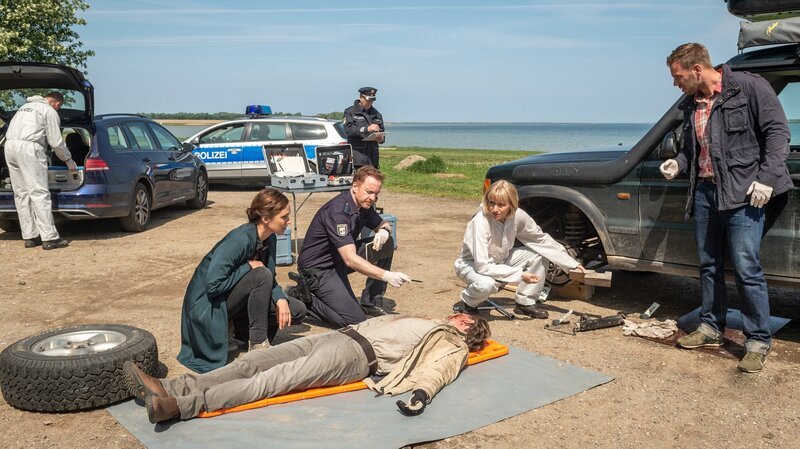 Ein neuer Fall für die Kollegen Joost (Nike Fuhrmann, 2.v.l.), Pöhlmann (Dominic Boeer, r.), Timmermann (Mathias Junge, 3.v.l.) und Roswitha Prinzler (Silke Matthias, 2.v.r.): Jemand hat den improvisierten Wagenheber von Andreas Hidde (Marco Wittorf, l.) weggetreten. Der Mann ist von seinem eigenen Wagen zerquetscht worden. Doch wer ist so wütend auf den Mann gewesen? Warum musste Andreas Hidde sterben? – Bild: ZDF und Marc Meyerbröker