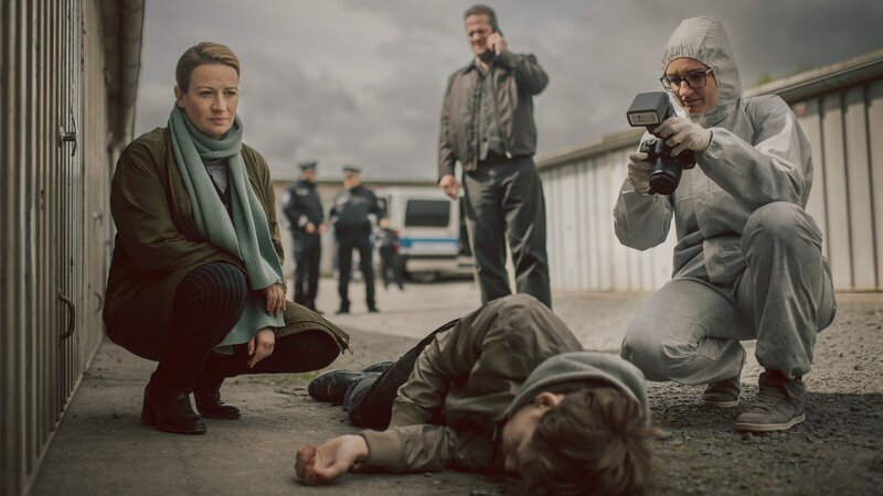Dr. Theresa Wolff (Nina Gummich, l.), Bruno Lewandowski (Aurel Manthei, M.) und die Spurensicherung (Komparsin, r.) verschaffen sich einen Eindruck von dem Tatort und der Leiche (Philip Günsch, liegend). – Bild: ZDF und ADRIAN GROSS