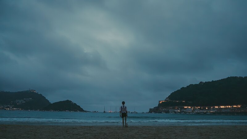 Ein Junge in einem Fußballtrikot steht auf einem Ball am Meer. – Bild: Beta Entertainment Spain 2023
