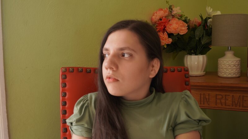 Medium shot of Natalia wearing a green shirt from intv. Sitting in red chair, looking to her right – Bild: Warner Bros. Discovery, Inc. or its subsidiaries and affiliates