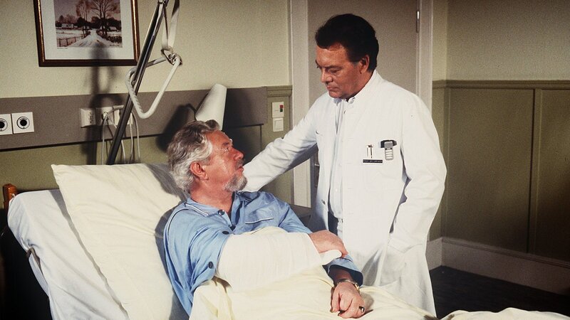 Der Patient Willi Anschütz (Klaus Havenstein, l.) soll am Blinddarm operiert werden. Aber je näher der Termin rückt, desto mulmiger wird ihm ums Herz. Prof. Brinkmann (Klausjürgen Wussow) versucht ihn zu überzeugen, dass er die Operation dringend benötigt. – Bild: ZDF und Thomas Waldhelm
