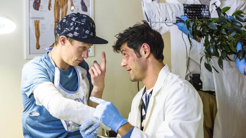 Kevin (Vincent Krüger, l.) hat sich beim Junggessellenabschied den Arm gebrochen und Sven (Michael Raphael Klein) muss den Arm eingipsen. – Bild: TVNOW /​ Julia Feldhagen
