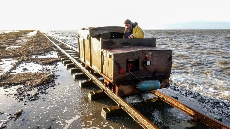 Postschiffer Johann Petersen transportiert die Weihnachtspakete. Bei Flut schwappt die Nordsee über den Lorendamm. – Bild: NDR/​Manfred Uhlig
