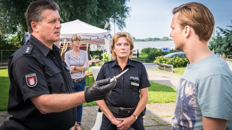 Hans (Bruno F. Apitz, l.) hat im Kofferraum von Benedikts (Jan Dose, r.) Hochzeitslimousine ein Springmesser gefunden und stellt ihn zur Rede. Benedikt bestätigt zwar, dass es sein Messer ist, schwört aber, dass er es nicht in den Kofferraum gelegt hat. Regine Schulz (Esther Esche, 2.v.l.) und Claudia (Janette Rauch, 2.v.r.) beobachten Benedikt. – Bild: ZDF und Boris Laewen
