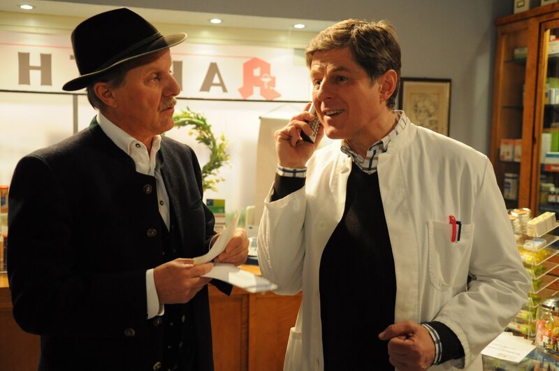 Bamberger dankt Flori per Telefon für seine Unterstützung bei der Internetseite seiner Apotheke. Von links: Lorenz Schattenhofer (Werner Rom) und Roland Bamberger (Horst Kummeth). – Bild: BR/​Jo Bischoff