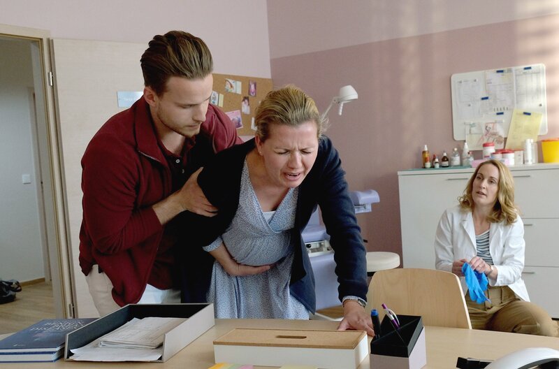 Bei Sabine Ellerbrock (Jessica Boehrs, M.) ist plötzlich die Fruchtblase geplatzt. Mark Kirchner (Nicolas Wolf, l.) begleitet die hochschwangere Patientin ins Sprechzimmer von Tanja Ewald (Christina Athenstädt, r.). – Bild: ARD/​Jacqueline Krause-Burberg