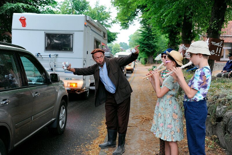 Kunos (Sven Walser) Versuch aus dem Stau Nennwert zu ziehen, mit Dosenwerfen und Flötenspiel. – Bild: NDR/​Nicolas Maack