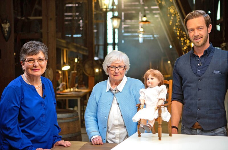 Sigrid Öhl (li.) bringt Gastgeber Arndt Reisenbichler (re.) eine mehr als hundert Jahre alte Porzellanpuppe mit. Puppenmacherin Liselotte Gorwicz (Mitte) prüft, ob die Puppe noch zu retten ist. – Bild: SWR/​AV MEDIEN