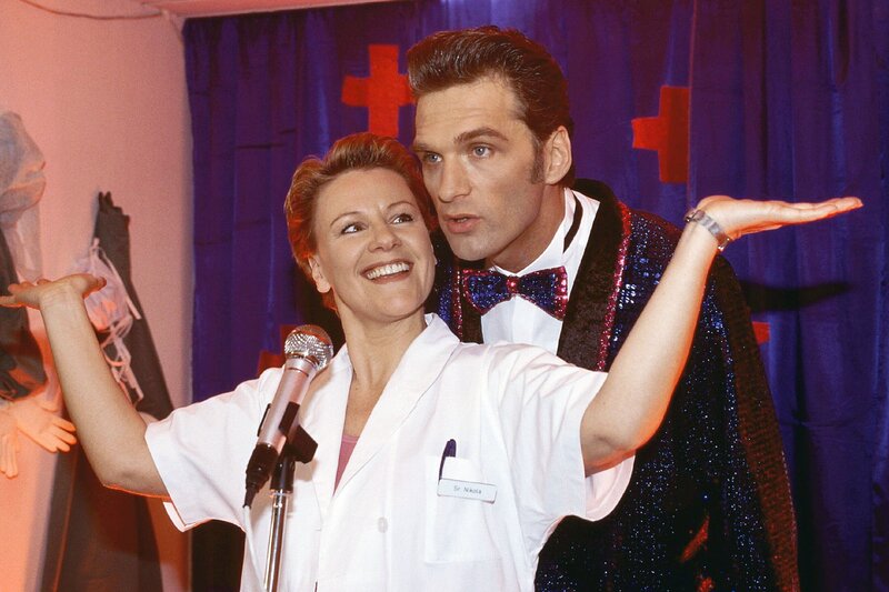 „Tag der offenen Tür“ im Krankenhaus. Nikola (Mariele Millowitsch) und Schmidt (Walter Sittler) begeistern das Publikum mit einem mehr oder weniger spontanen Auftritt. – Bild: TVNOW /​ Guido Engels