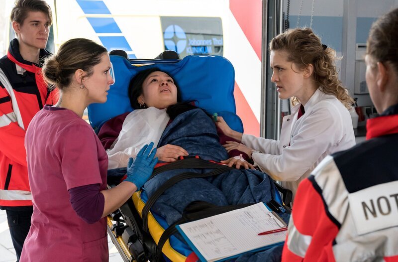 Dr. Winter Elly Winter (Juliane Fisch, r.) und Viktoria Stadler (Isabella Krieger, 2.v.l. mit Komparse, l.) nehmen Luna Reinhard (Andrea Guo, M.) auf. Sie wird mit einer Unterarmfraktur und Schürfwunden ins Johannes-Thal-Klinikum eingeliefert. – Bild: ARD/​Jens-Ulrich Koch