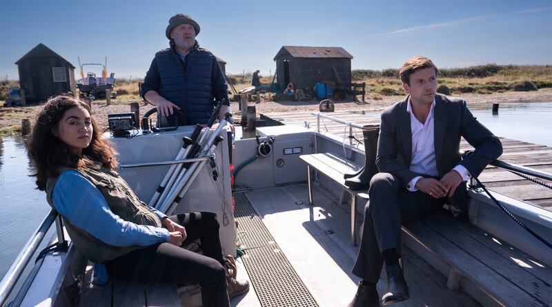 Sergeant Barbara Havers (Sofia Barclay) und Inspector Thomas Lynley (Leo Suter) setzen mit dem Fährmann Tony Shannon (Andrew Redman, re.) auf die Privatinsel über. – Bild: Playground Entertainment