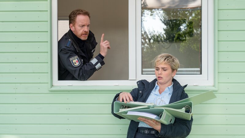 Die beiden sind einfach ein gutes Team: Polizeihauptmeister Timmermann (Mathias Junge, l.) und die dänische Austauschpolizistin Stine Bergendal (Sidsel Hindhede, r.) werden in dem Tiny House des Opfers Doris Petersen fündig. Hier sind allerhand Unterlagen, die sie mit ins Revier nehmen können. Vielleicht findet sich hier ein Hinweis auf einen möglichen Täter? Warum musste Doris Petersen sterben? Bei wem hat sie in der Garage zu viel aufgeräumt? – Bild: ZDF /​ Meyerbroeker