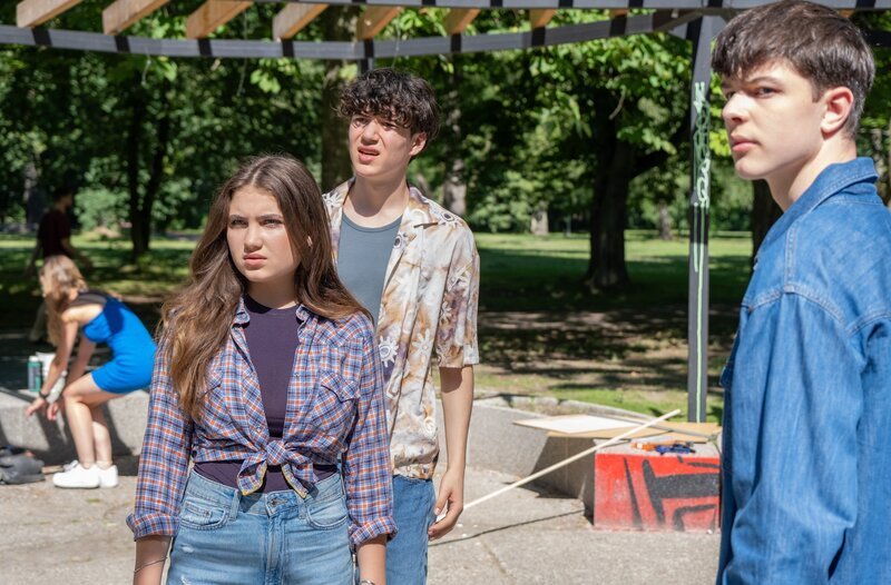 Hanna (Helena Pieske, li.), Till (Arthur Gropp, mi.) und ihre Freunde bereiten im Park Plakate für eine Klimademo vor. Hanna hat gehofft, dass das, wenn Cosmo (Max Bär, re.) auch dazukommt und mitmacht, ihre Freundschaft wieder etwas belebt. Doch Cosmo hat nur seine Crypto-Idee im Kopf und ist die ganze Zeit am Handy. Doch dann tauchen plötzlich ein paar Jungs auf und fangen an zu pöbeln. – Bild: MDR/​Saxonia Media/​Sebastian Kiss