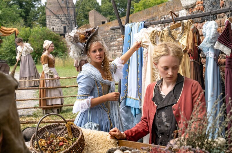 Prinzessin Josefine (Lucie Hollmann) entdeckt auf dem Markt die schönen Kleider von Helene (Caroline Hellwig). – Bild: WDR/​Wolfgang Ennenbach